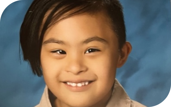A young person with dark hair and a wide smile looks straight ahead against a blue background.