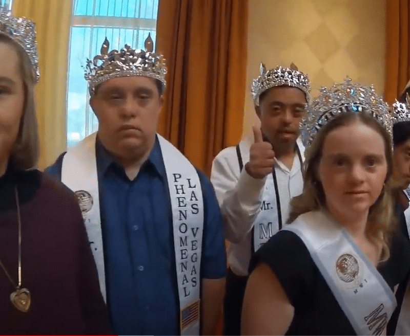 A group of people wearing crowns and sashes, with one man giving a thumbs-up and "PHENOMENAL LAS VEGAS" visible.