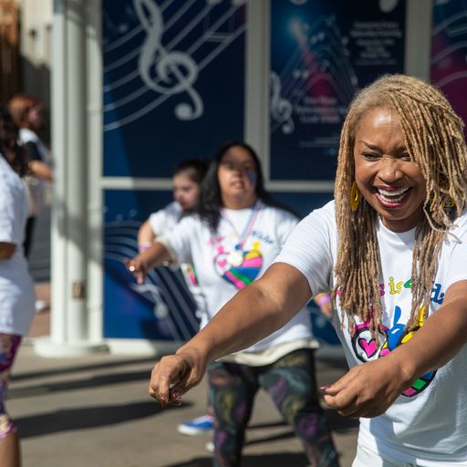 A woman with blonde dreadlocks and a "Music is Life" t-shirt laughs while dancing outdoors.