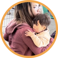 A young woman with glasses holds a sleeping child with dark hair against her shoulder.