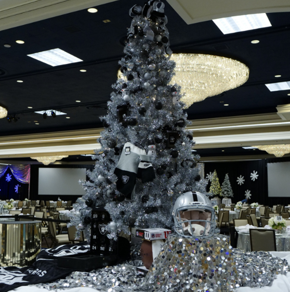 A silver tinsel Christmas tree decorated with black and silver ornaments, socks, and an NFL helmet.