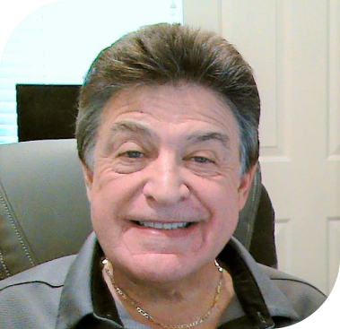 A smiling man with dark hair and a gold chain wears a gray collared shirt.