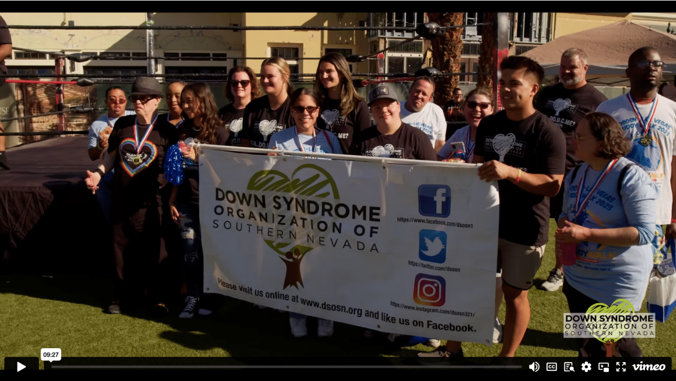 A diverse group of people hold a banner that reads "Down Syndrome Organization of Southern Nevada."
