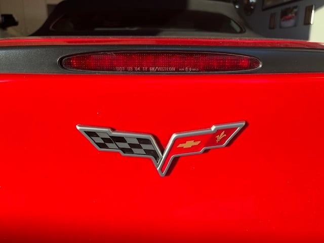 A red Corvette's rear with a "DOT US 04 1Y GM/VISTEON" brake light and a silver emblem.